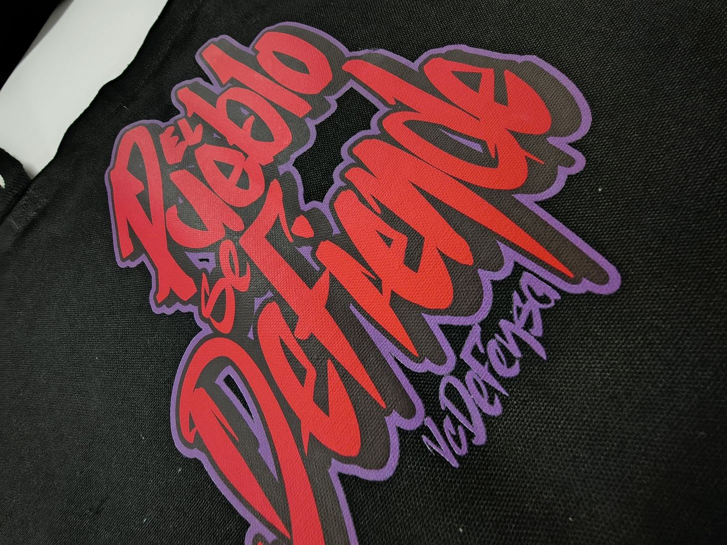 Red and purple graffiti lettering with the VC Defensa signature, printed on black fabric.